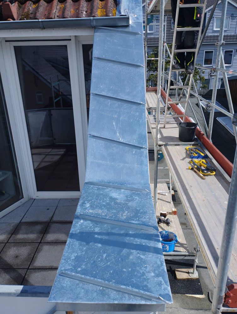 Metallblech an der Gebäudekante mit diagonalen Nähten, von oben betrachtet; ein Dach und ein Gerüst sind zu sehen.