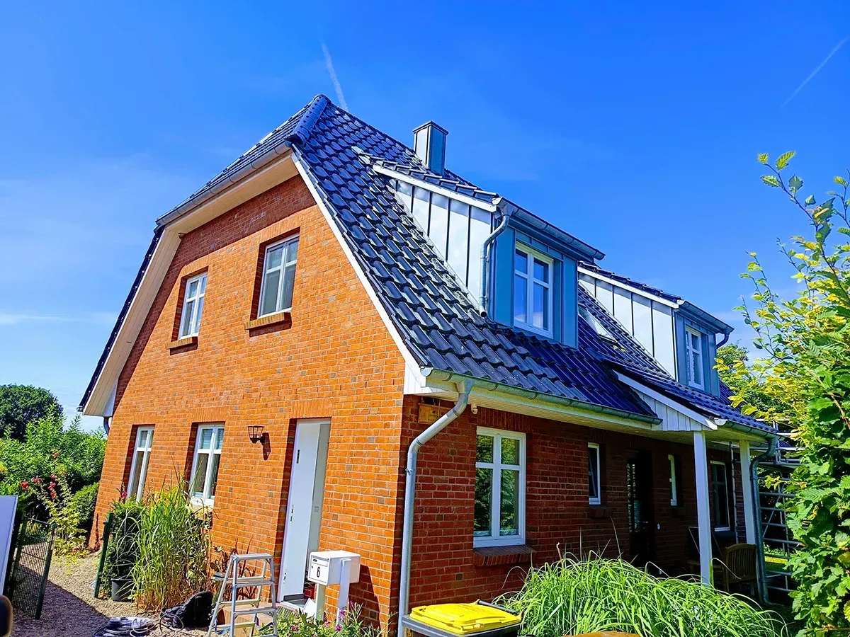 Eine Kupferrinne mit einem Loch sitzt auf einem Wellblechdach. Wassertropfen sind zu sehen.