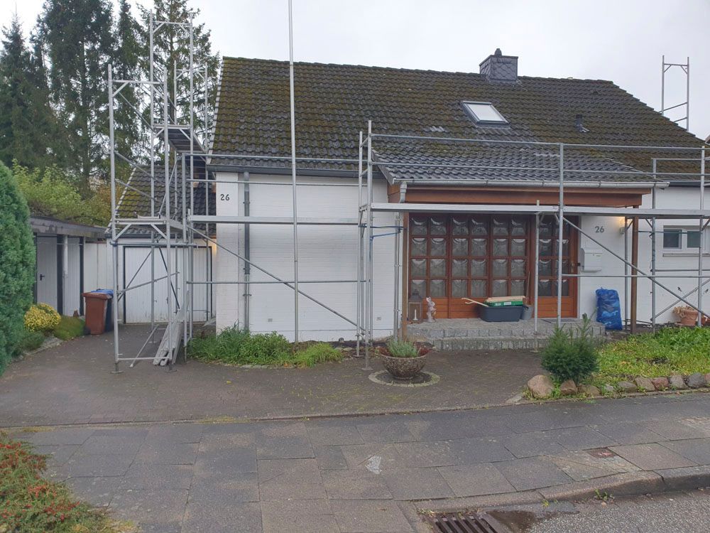 Hausfassade mit Gerüst. Bewölkter Himmel. Graue Betonauffahrt.