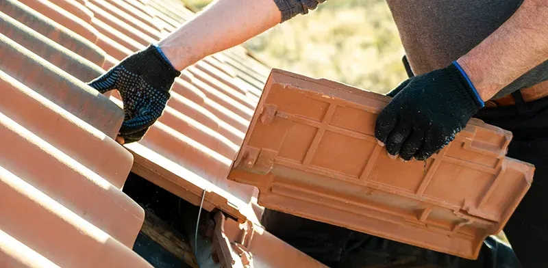 Eine Person verlegt einen Terrakotta-Dachziegel auf einem Dach mit sonnenbeschienenen Ziegeln.