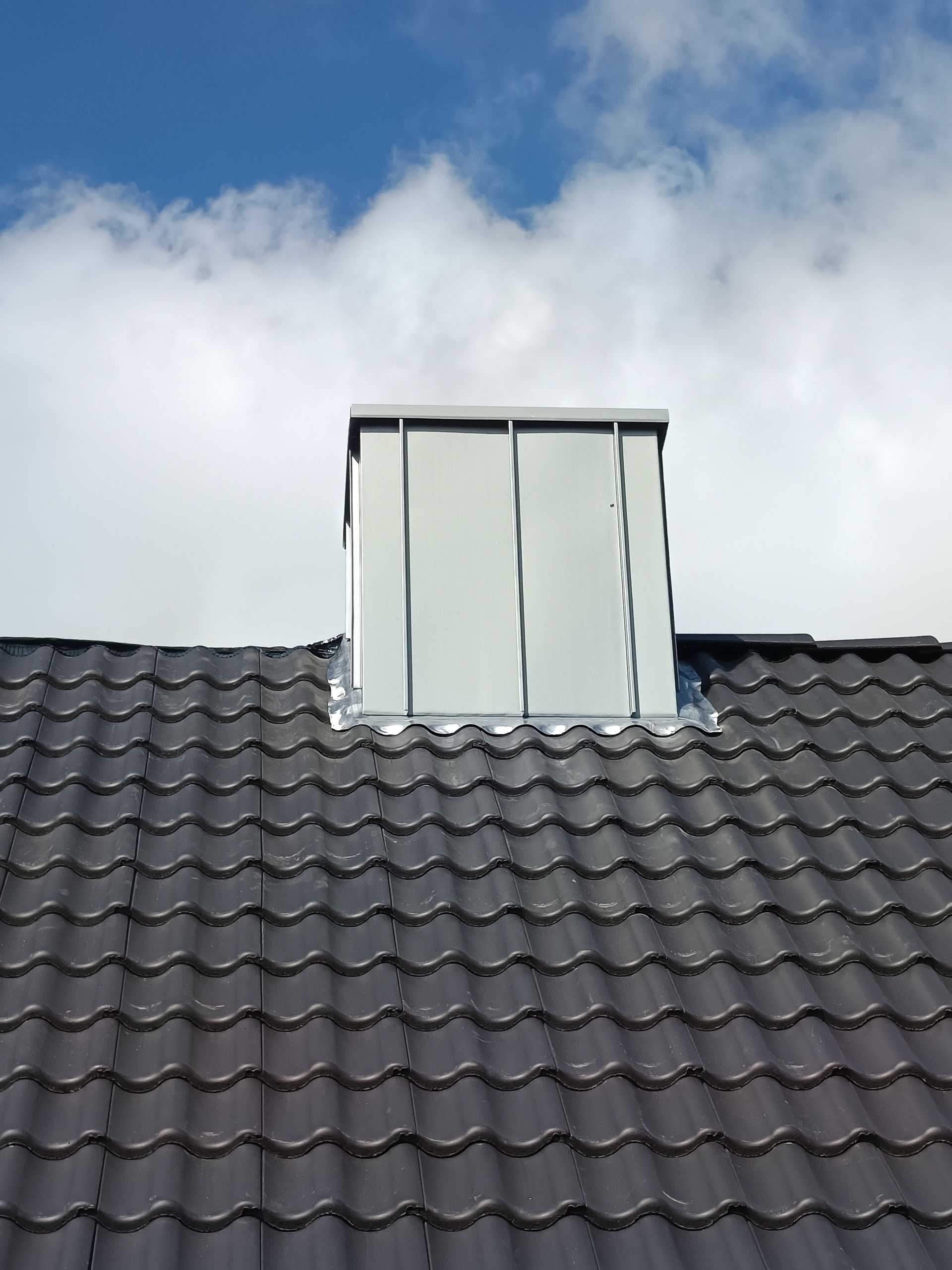 Rotes Ziegeldach mit gemauertem Schornstein vor blauem Himmel.