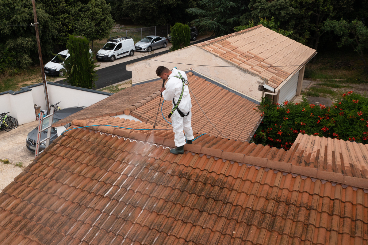 Un artisan qui démousse un toit avec un jet d'eau