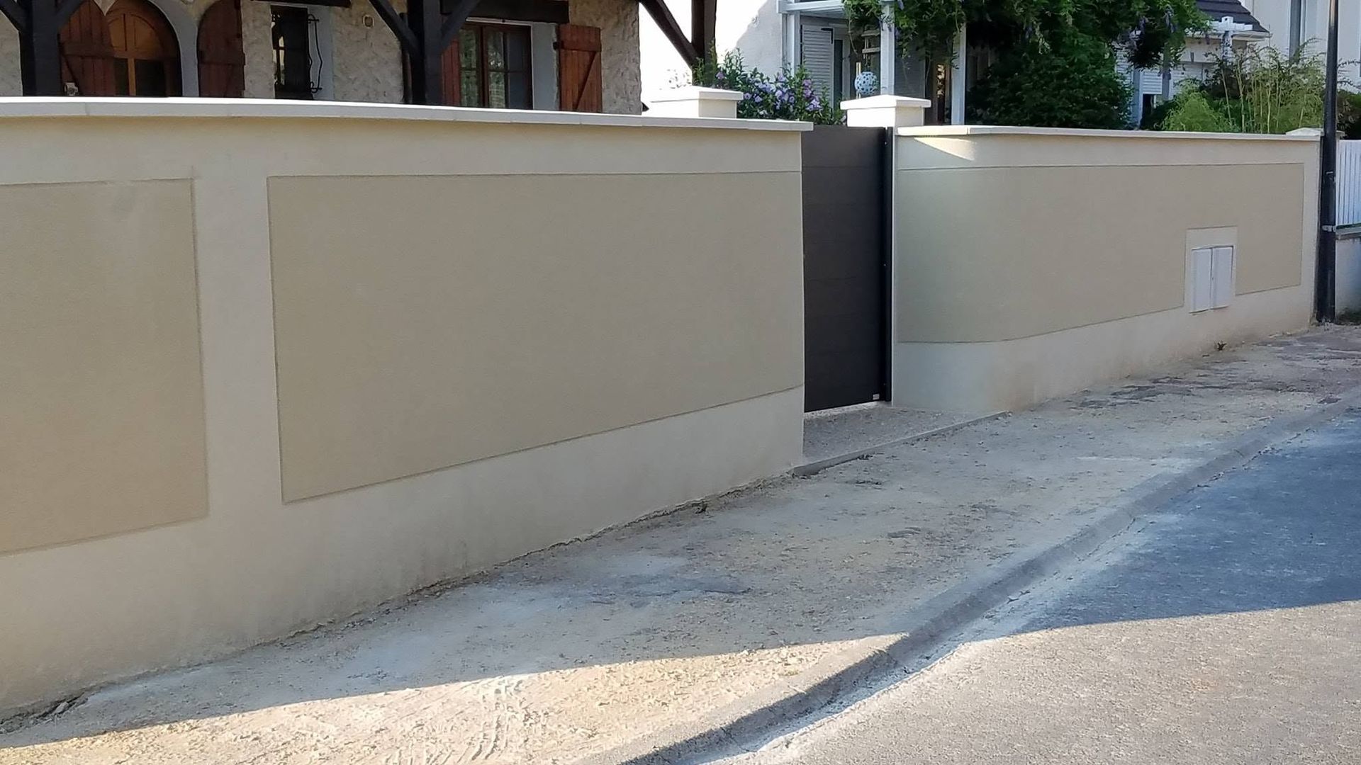 Mur en stuc beige avec un portail sombre dans une rue résidentielle calme.