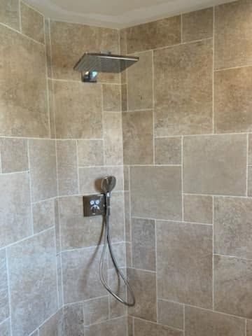 Douche moderne carrelée avec pommeau de douche effet pluie chromé et douchette à main.