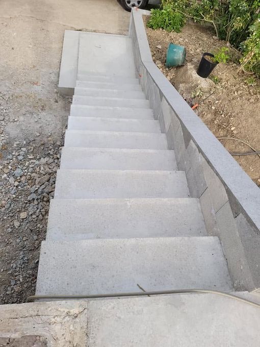 Escalier extérieur en béton avec un mur de soutènement incurvé bordant un chemin de terre, et des seaux en haut.