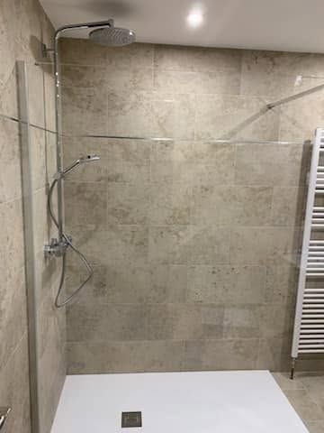 Douche à l’italienne moderne carrelée, avec paroi vitrée et pommeau de douche mural.