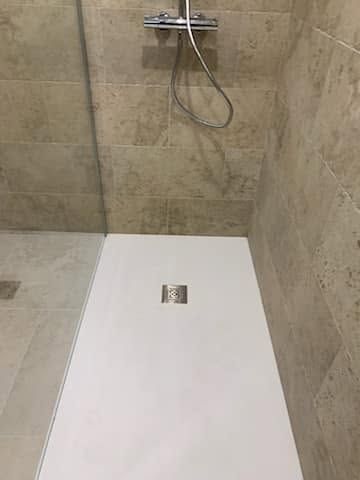 Douche moderne avec sol blanc, murs carrelés beige et pommeau de douche mural.