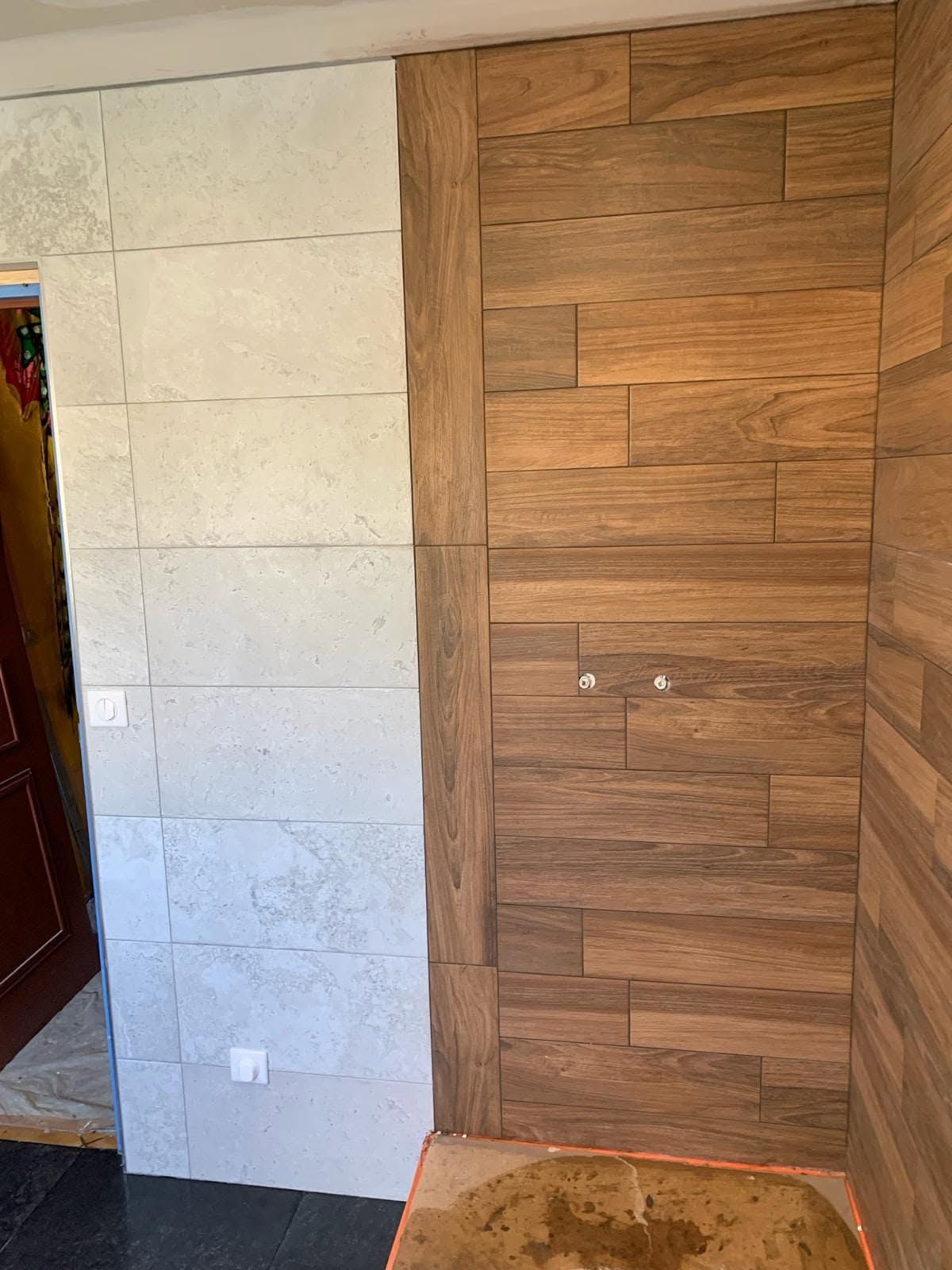 Mur intérieur avec des carreaux de pierre blanche, à côté d’un mur d’accent lambrissé de bois brun et d’une porte.