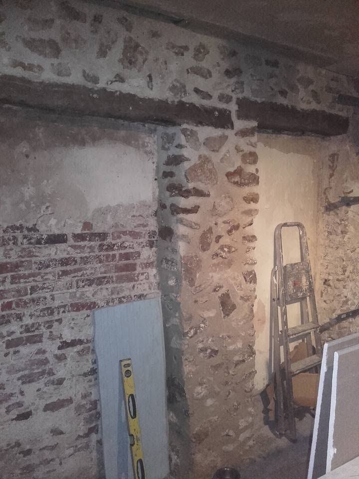 Mur intérieur en pierre avec des briques apparentes, une échelle et des panneaux empilés dans une zone en rénovation.