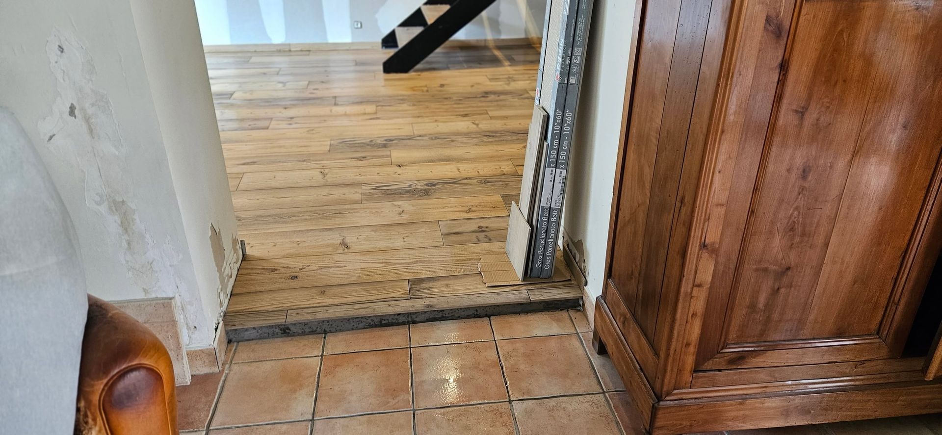 Seuil entre l’entrée carrelée et un parquet, près d’une armoire en bois et d’un mur blanc.