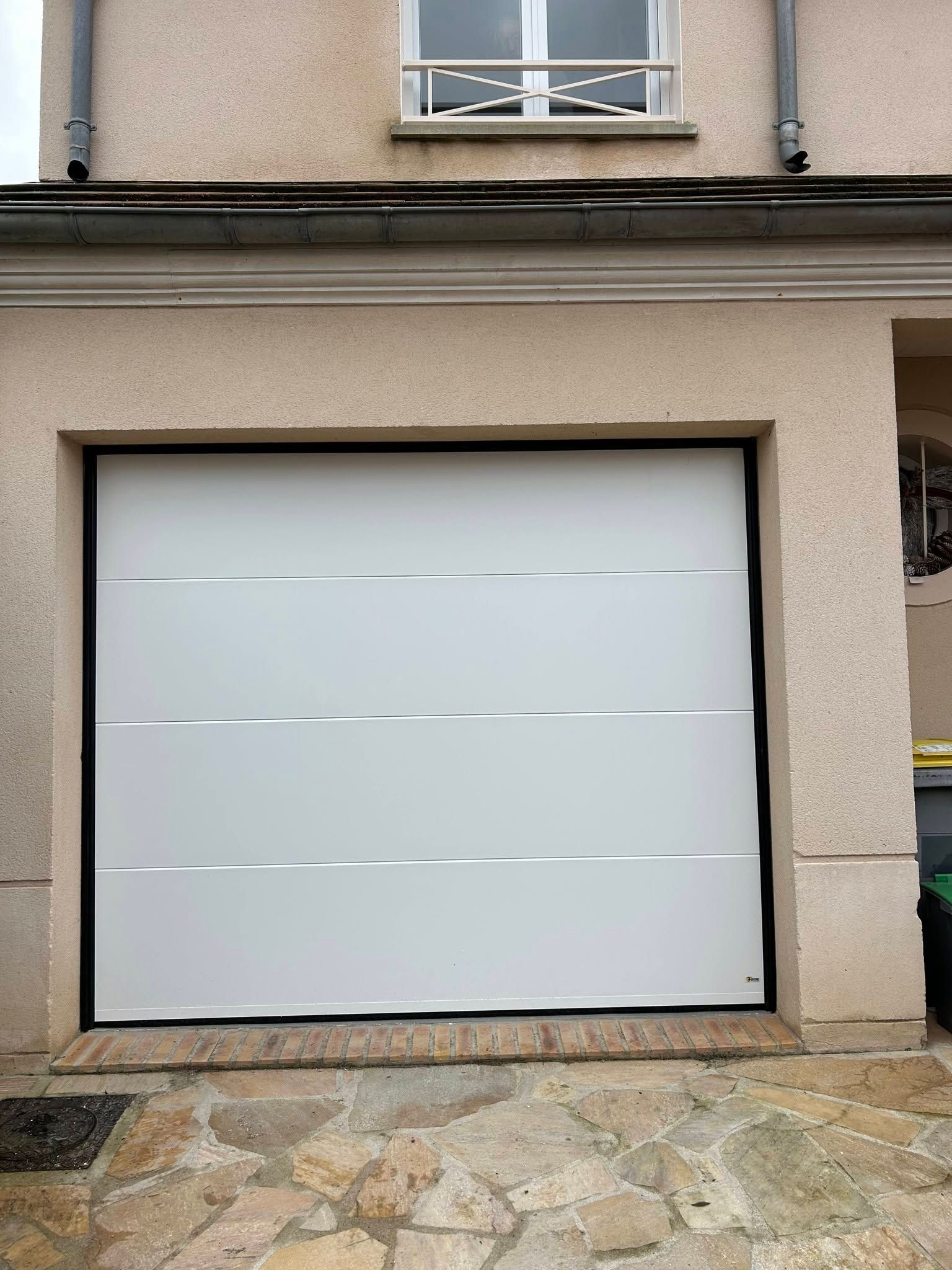 Porte de garage blanche fermée sur la façade beige d’un bâtiment.