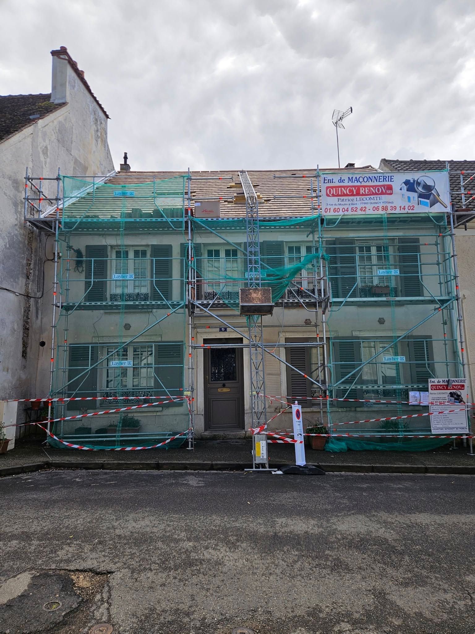 Bâtiment de deux étages en cours de rénovation, recouvert de filets de sécurité verts et d’échafaudages.