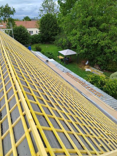 Structure au toit jaune donnant sur un jardin verdoyant avec des arbres, du mobilier de jardin et un petit parasol de terrasse.