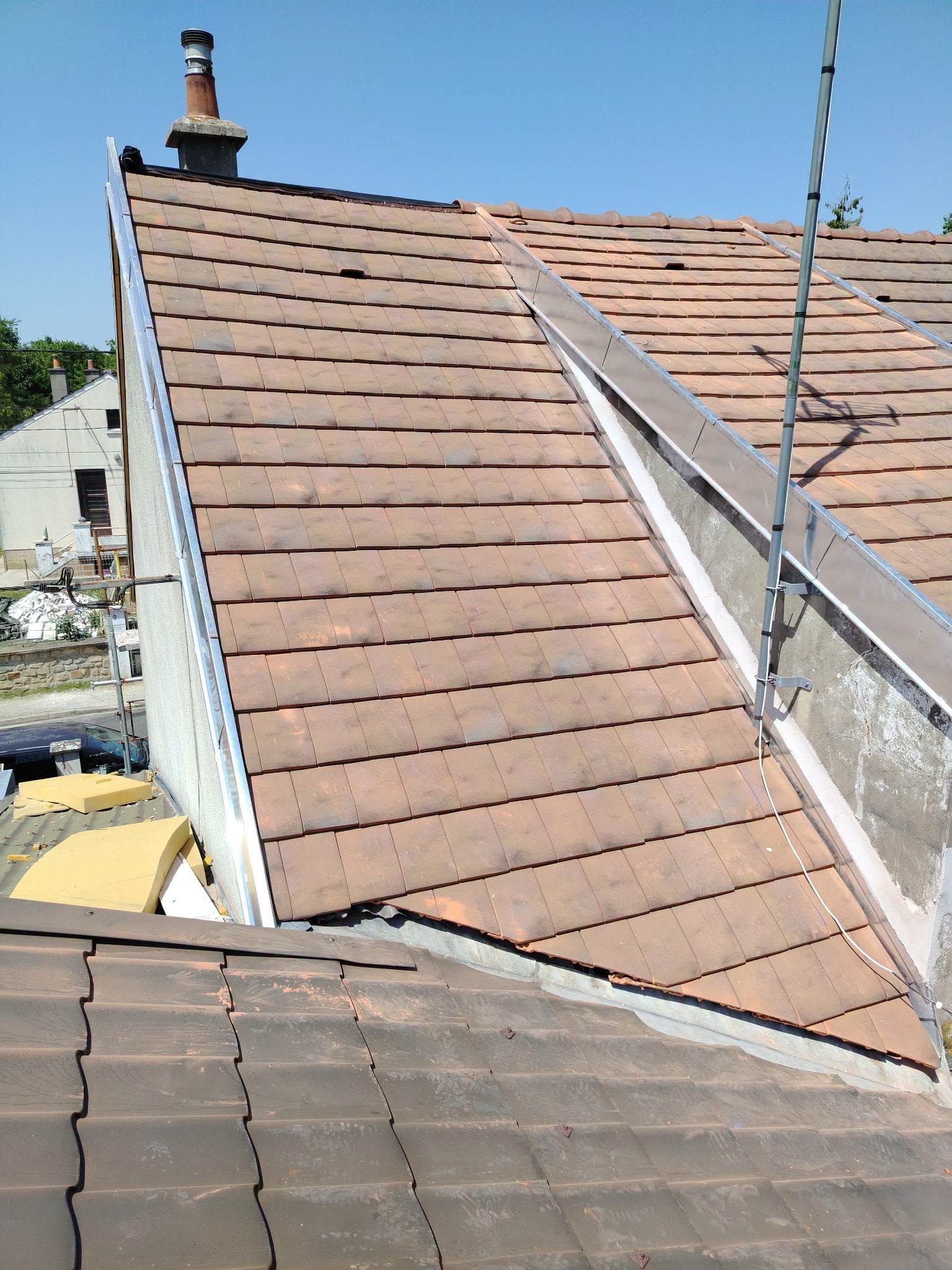 Toit en pente couvert de bardeaux bruns et doté d’une rambarde blanche, vu d’en haut pendant des travaux de toiture.