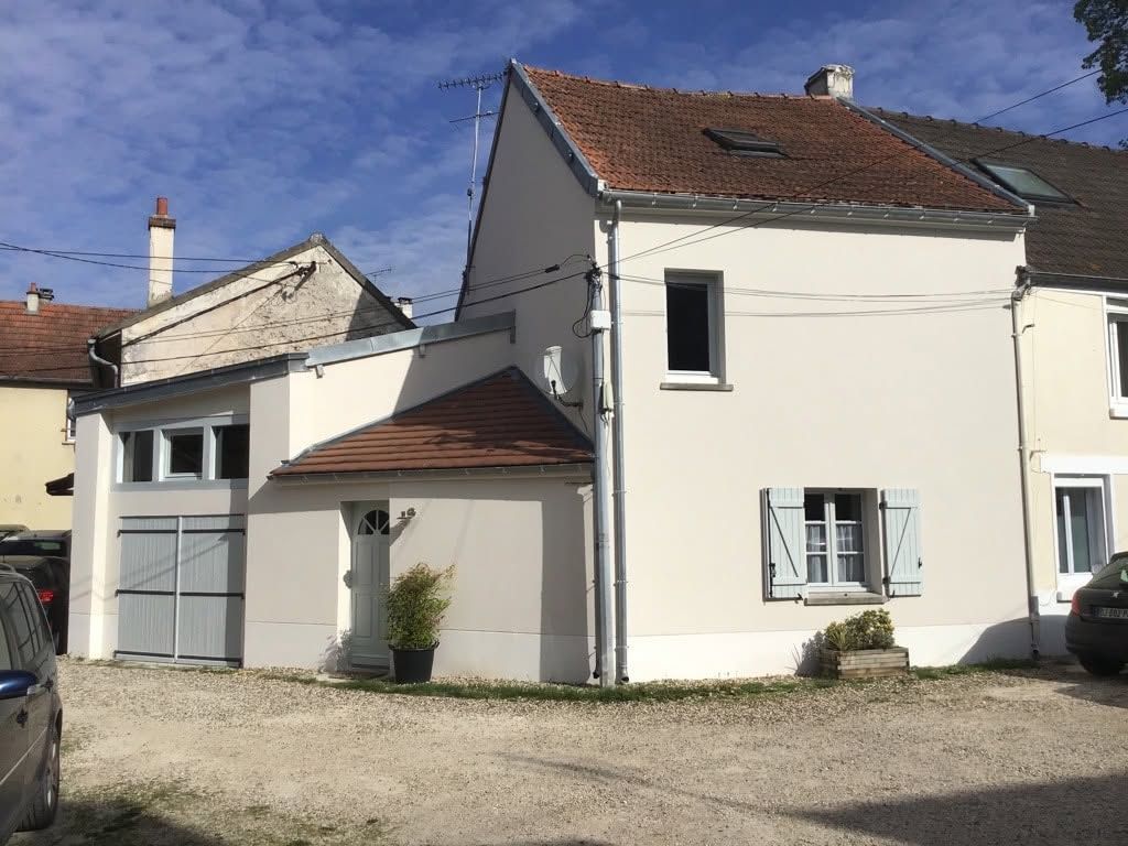 Maison blanche à deux étages avec un toit rouge et un garage attenant, dans une allée en gravier.