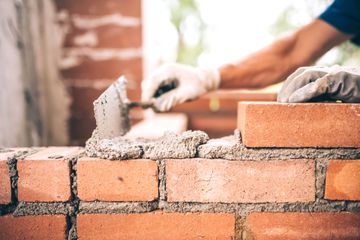 Des mains posent des briques rouges avec du mortier sur un mur en construction.