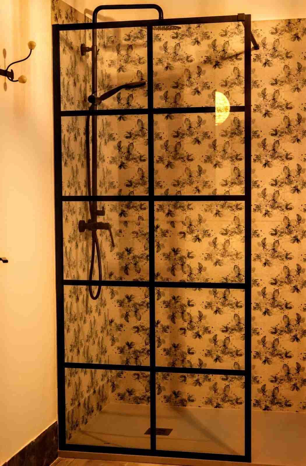 Estantería de metal negro junto a una pared empapelada con motivos florales, en una habitación con luz cálida