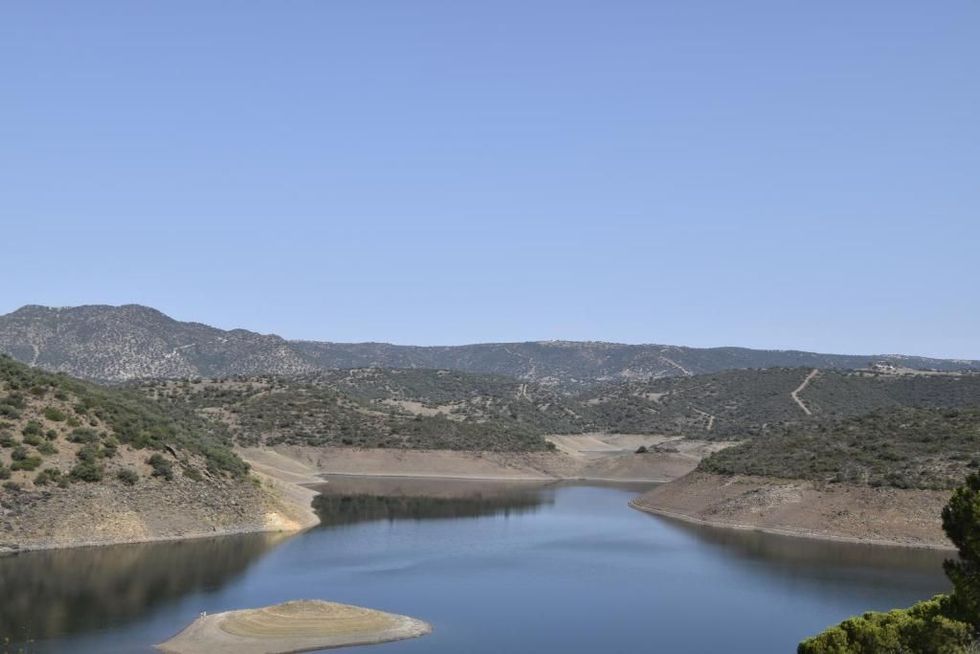 Un lago amplio de aguas tranquilas, orillas arenosas y colinas boscosas bajo un cielo azul despejado