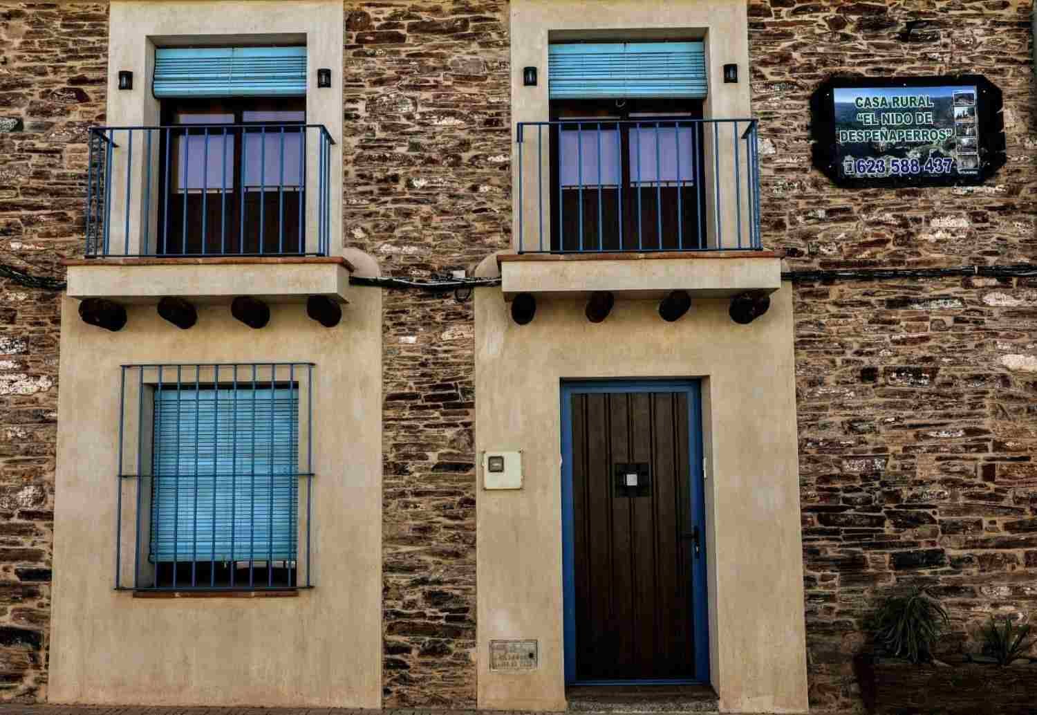 Fachada de piedra con ventanas de contraventanas azules, una puerta de madera y un pequeño letrero colgante.