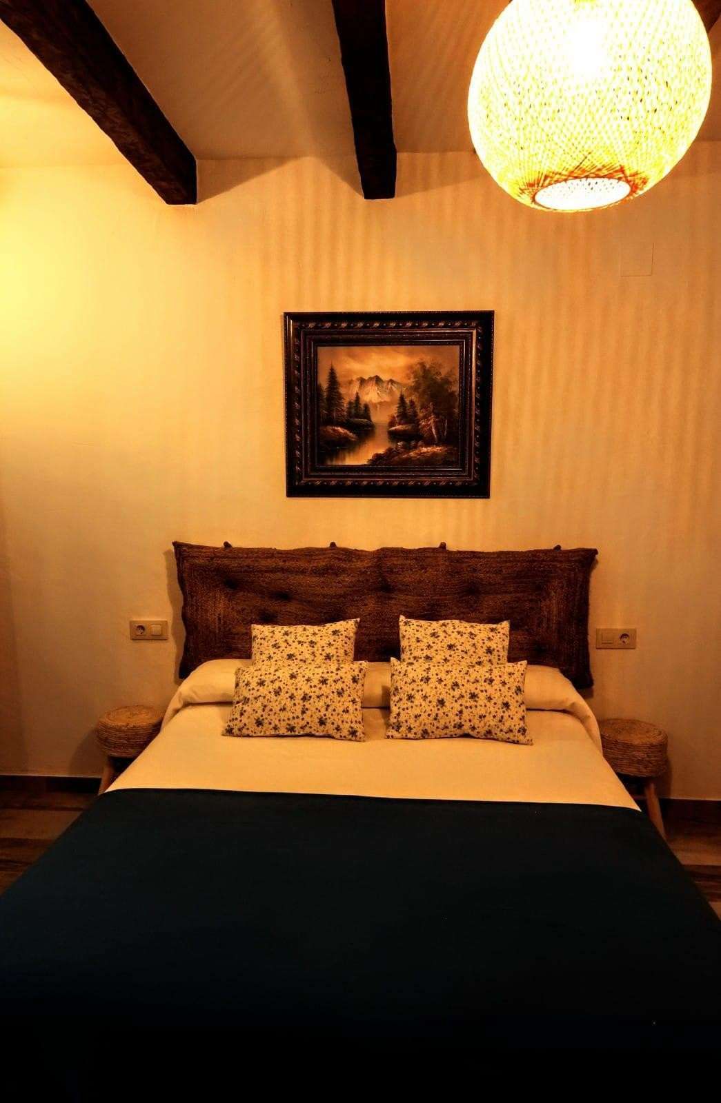 Dormitorio cálidamente iluminado, con una cama, cojines estampados, cuadros enmarcados en la pared.