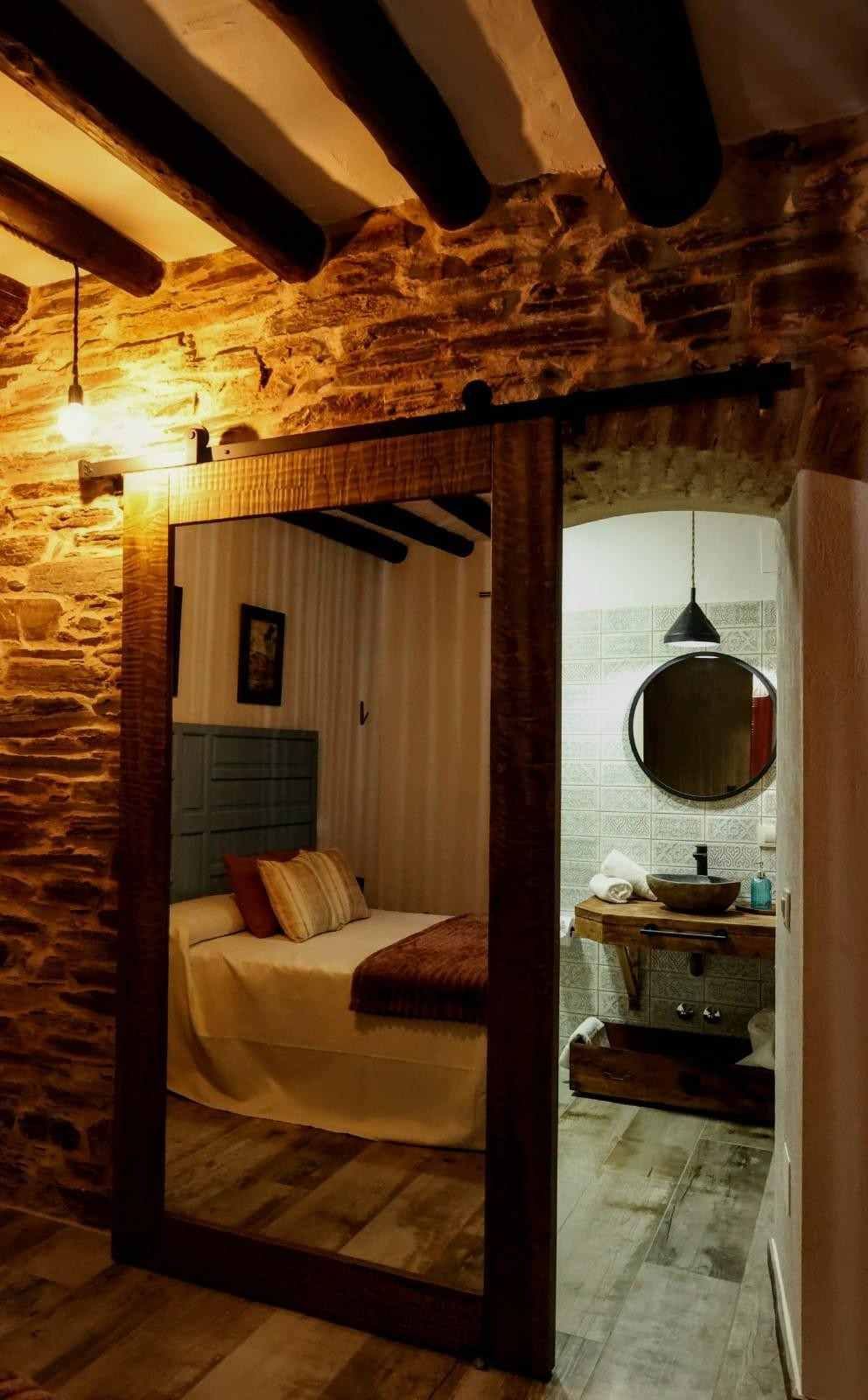 Acogedor dormitorio de estilo rústico visto desde una puerta, con paredes de piedra, vigas a la vista.