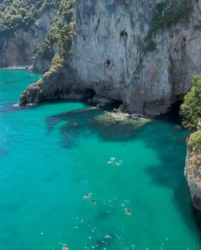 Cala de aguas turquesas con bañistas al pie de un empinado acantilado de piedra caliza blanca