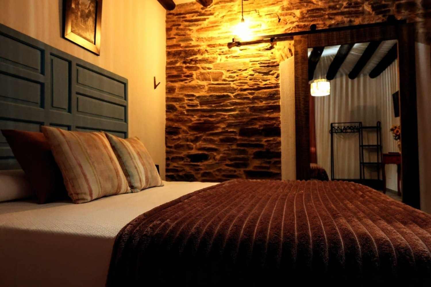 Dormitorio acogedor con cama, almohadas a rayas, iluminación cálida, pared de piedra y puerta abierta