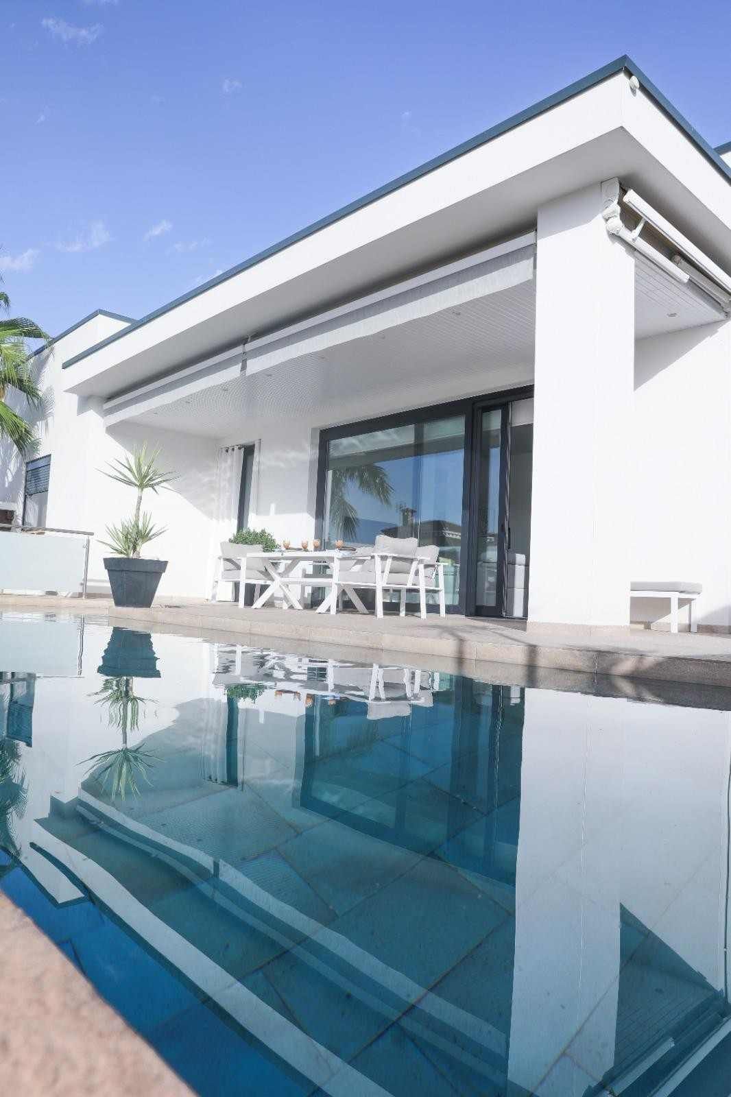 Casa moderna blanca con puertas de cristal y una piscina infinita que refleja la zona del patio