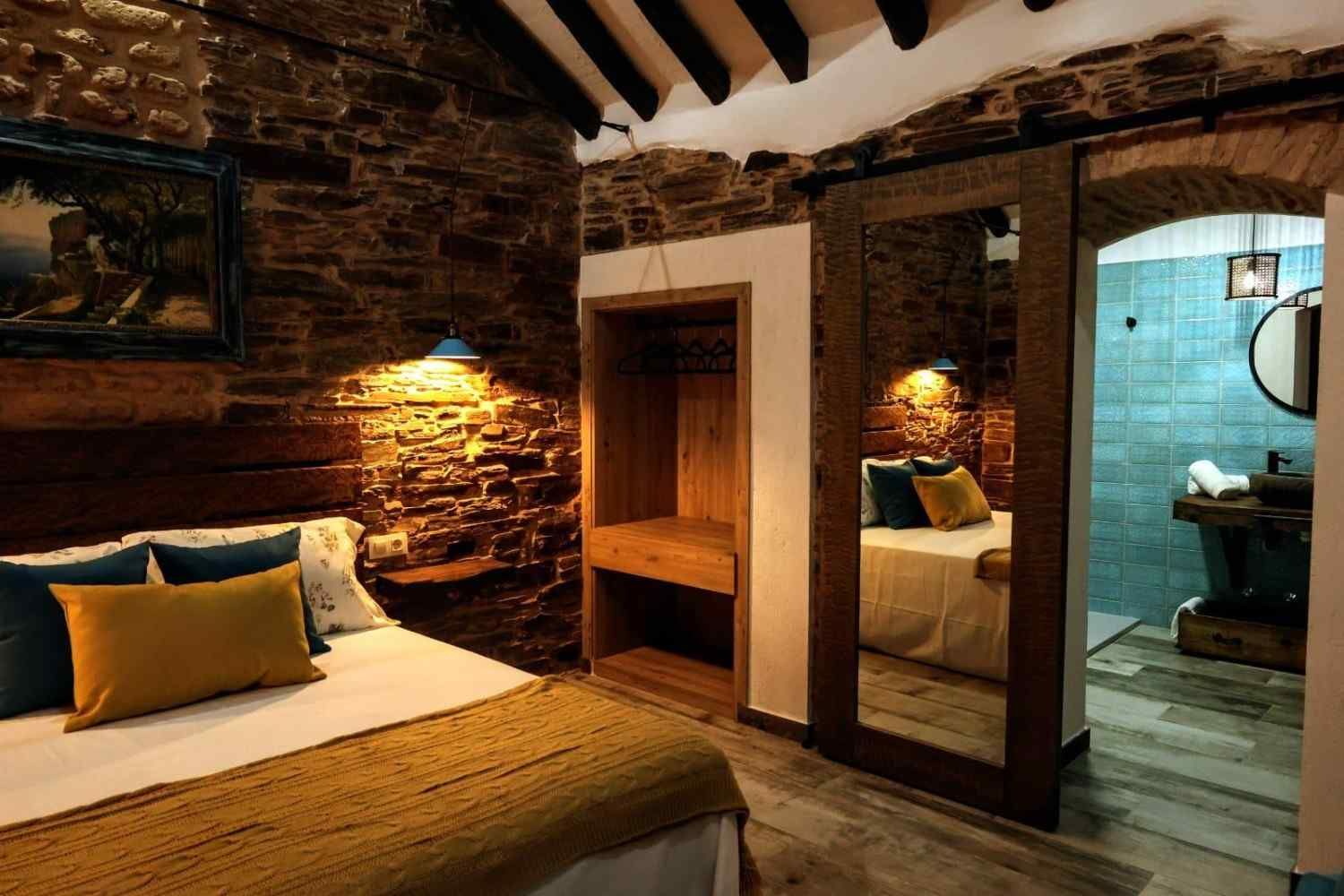 Dormitorio rústico con paredes de piedra, vigas de madera, cama y puerta al baño