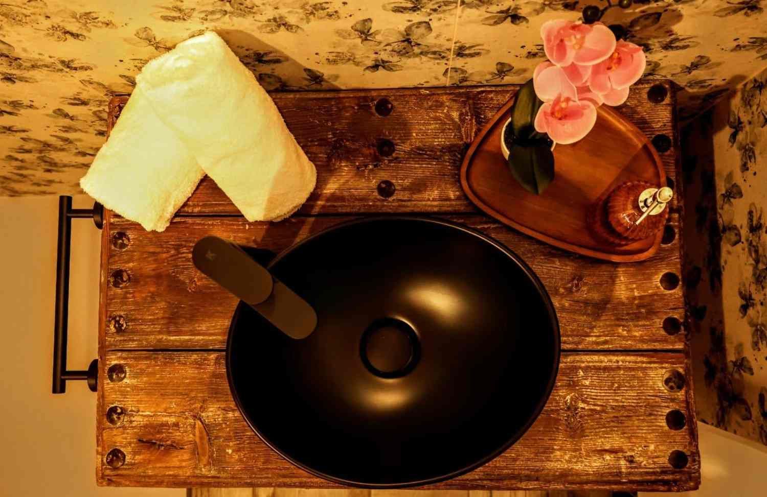 Bandeja de madera con un wok negro, una toalla blanca enrollada y pequeñas flores rosas sobre un fondo de tela estampada