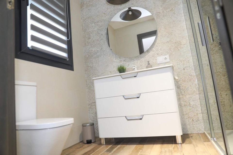 Baño pequeño con mueble de lavabo blanco, espejo redondo, inodoro y cabina de ducha.