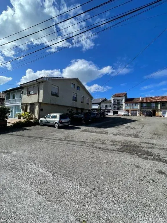 Calle residencial con coches aparcados, edificios bajos y un cielo azul intenso con nubes