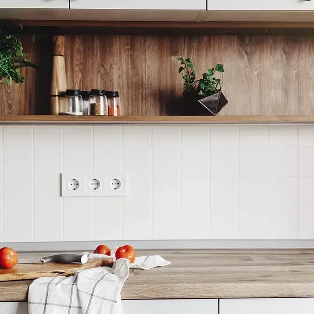 Encimera de cocina con salpicadero de azulejos blancos, estante de madera con especias, tomates y vegetación.