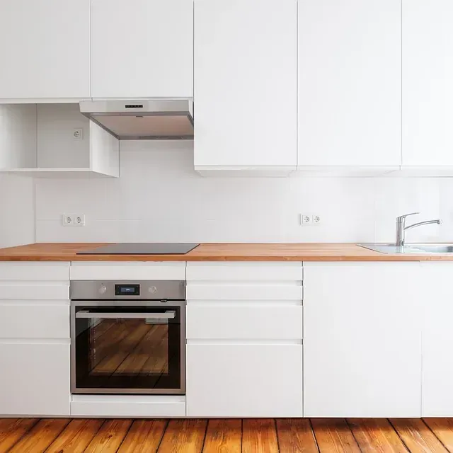 Cocina blanca con horno de acero inoxidable, encimera de madera y gabinetes.