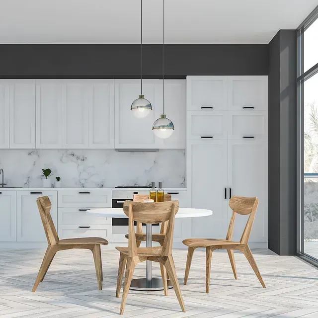 Cocina moderna con gabinetes blancos, mesa redonda, sillas de madera y lámparas colgantes.