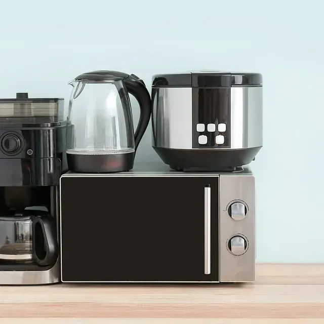 Cafetera, hervidor eléctrico, olla arrocera y microondas sobre una encimera de madera.