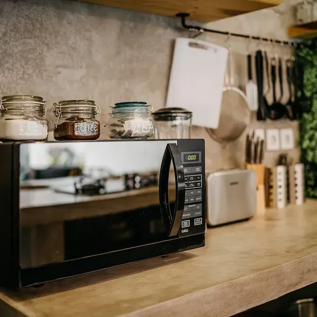 Microondas sobre una encimera con frascos, utensilios y una tostadora en un entorno de cocina.
