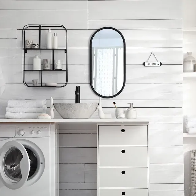 Baño con paredes blancas, lavadero, lavabo, espejo y detalles en negro.