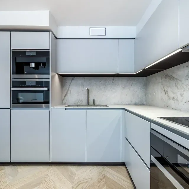 Cocina moderna de color azul claro con electrodomésticos integrados, salpicadero de mármol y suelo de madera.