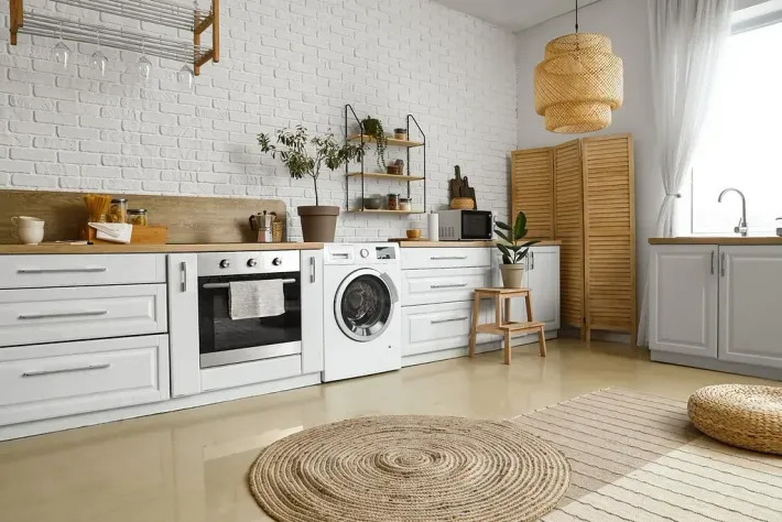 Una cocina luminosa con paredes de ladrillo blanco, detalles de madera y lavadora.