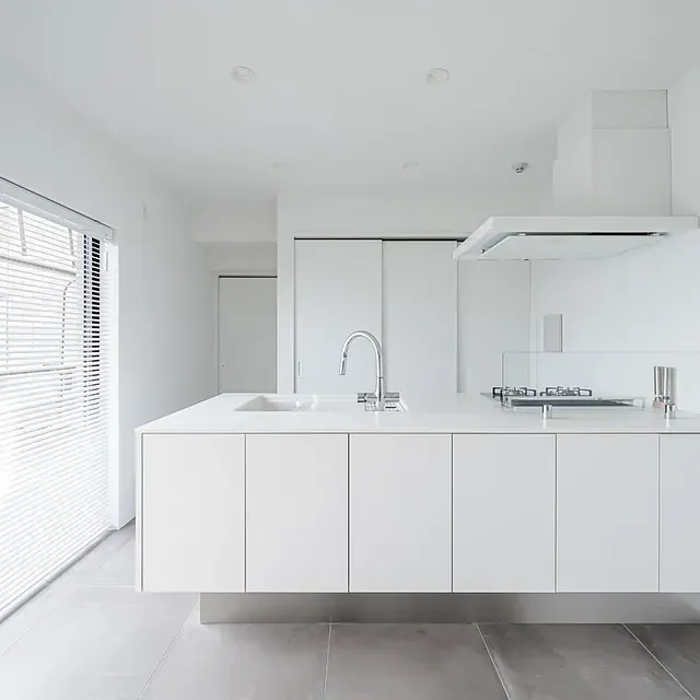 Cocina moderna totalmente blanca con isla, fregadero, anafe y ventana con persianas.
