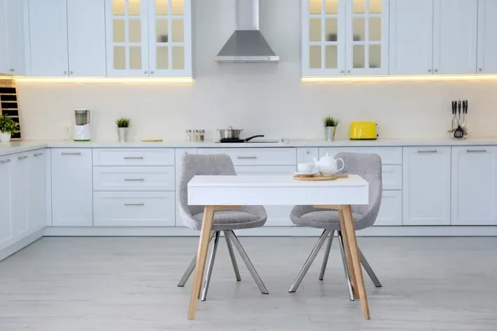 Cocina blanca con mesa y dos sillas. Armarios, estufa, tostadora y decoración.