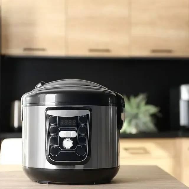 Olla a presión eléctrica sobre una mesa de madera en una cocina con gabinetes de madera clara y una pared negra.