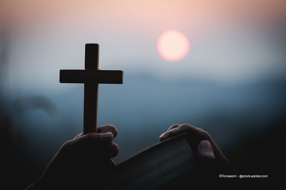 Eine Hand hält das Kreuz hoch, die andere hält die Bibel