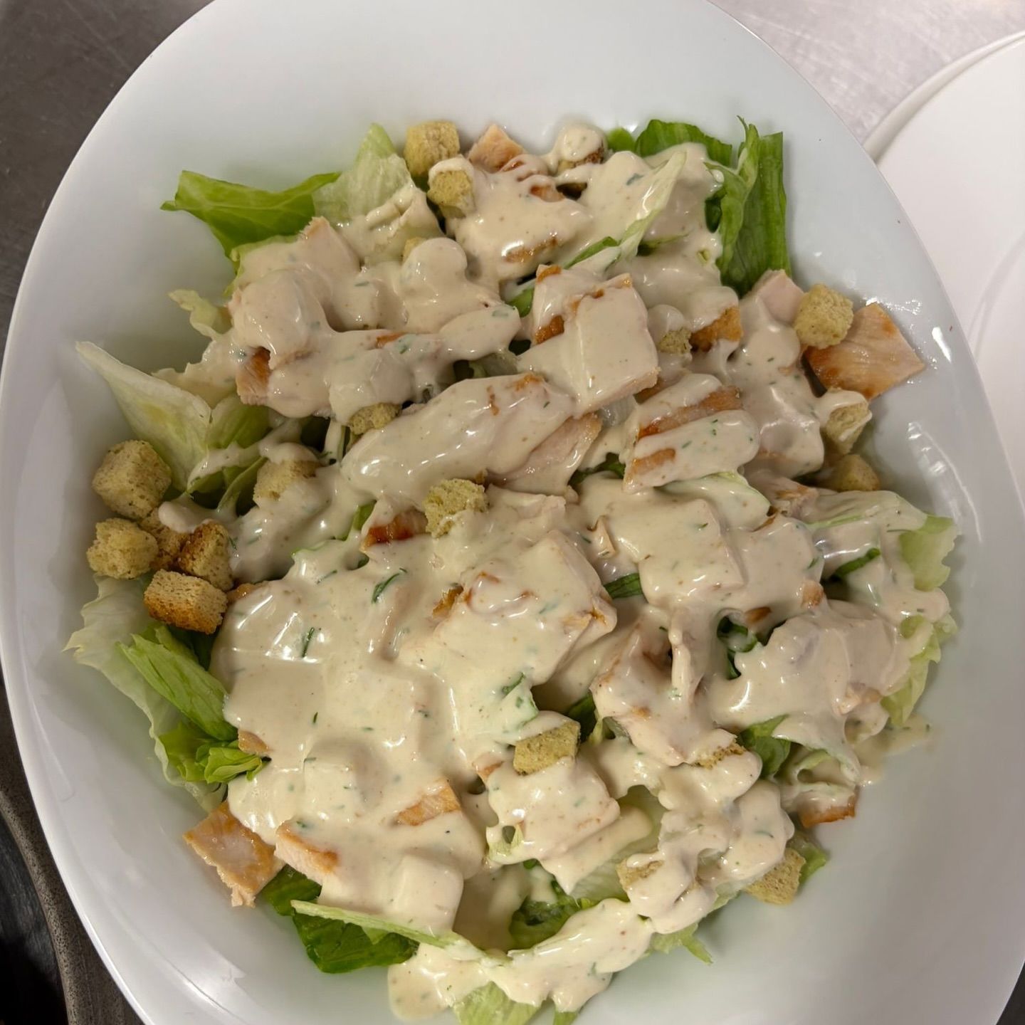 Caesar-Salat mit Croutons und Hähnchen in einer weißen Schüssel.