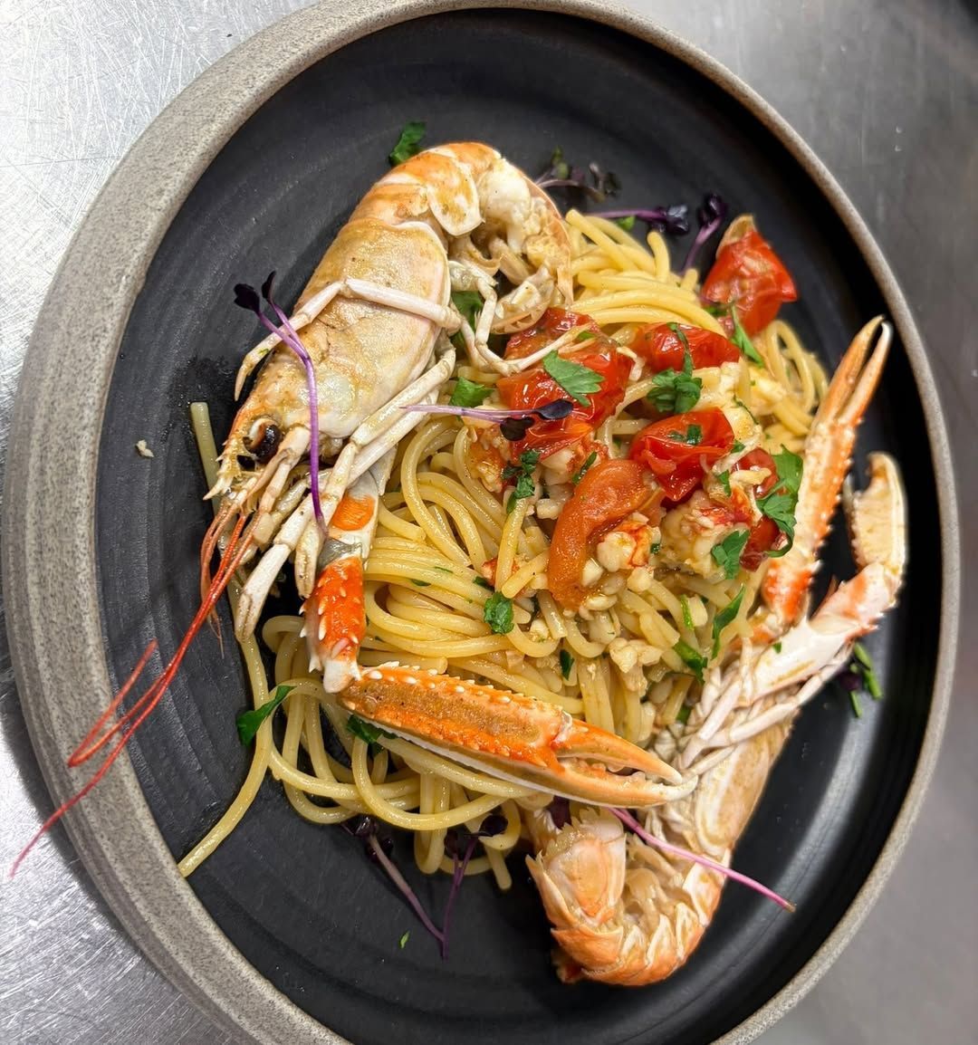 Spaghetti mit Scampi, gehackten Tomaten und Kräutern auf einem dunklen Teller.