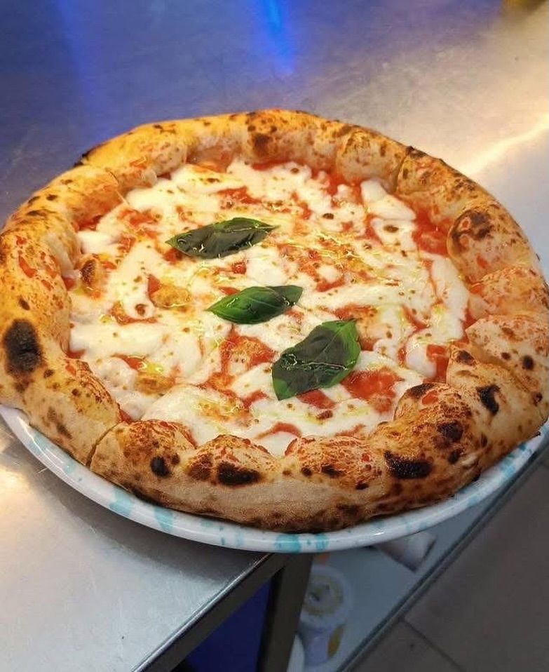 Neapolitanische Pizza auf einem Teller; angebrannter Rand, Tomatensauce, Mozzarella und Basilikumblätter.