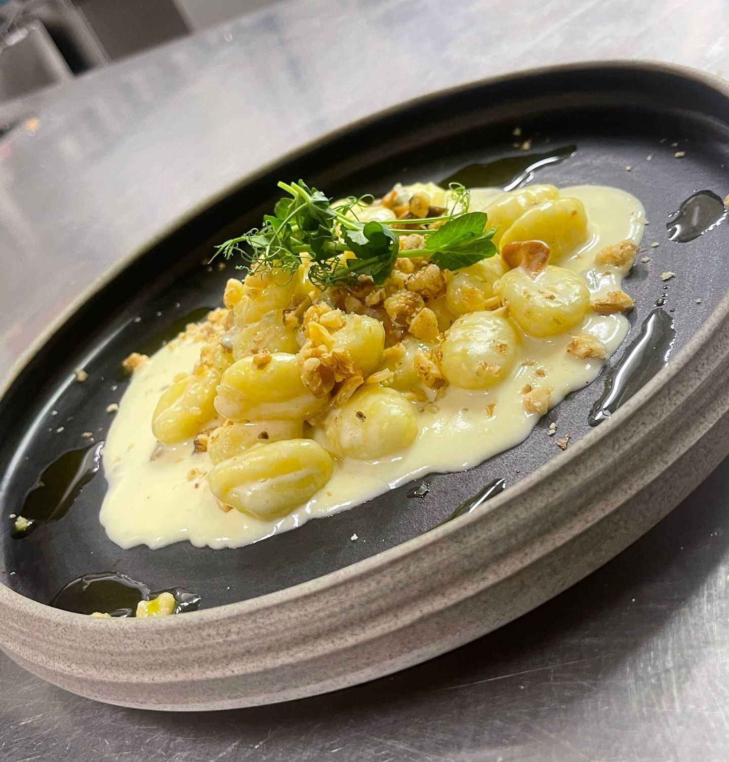 Gnocchi-Gericht auf einem dunklen, ovalen Teller mit cremiger Soße, Kräutern und gerösteten Krümeln.