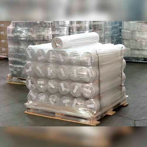 Palet de rollos de tela blanca envueltos en plástico transparente en un almacén.