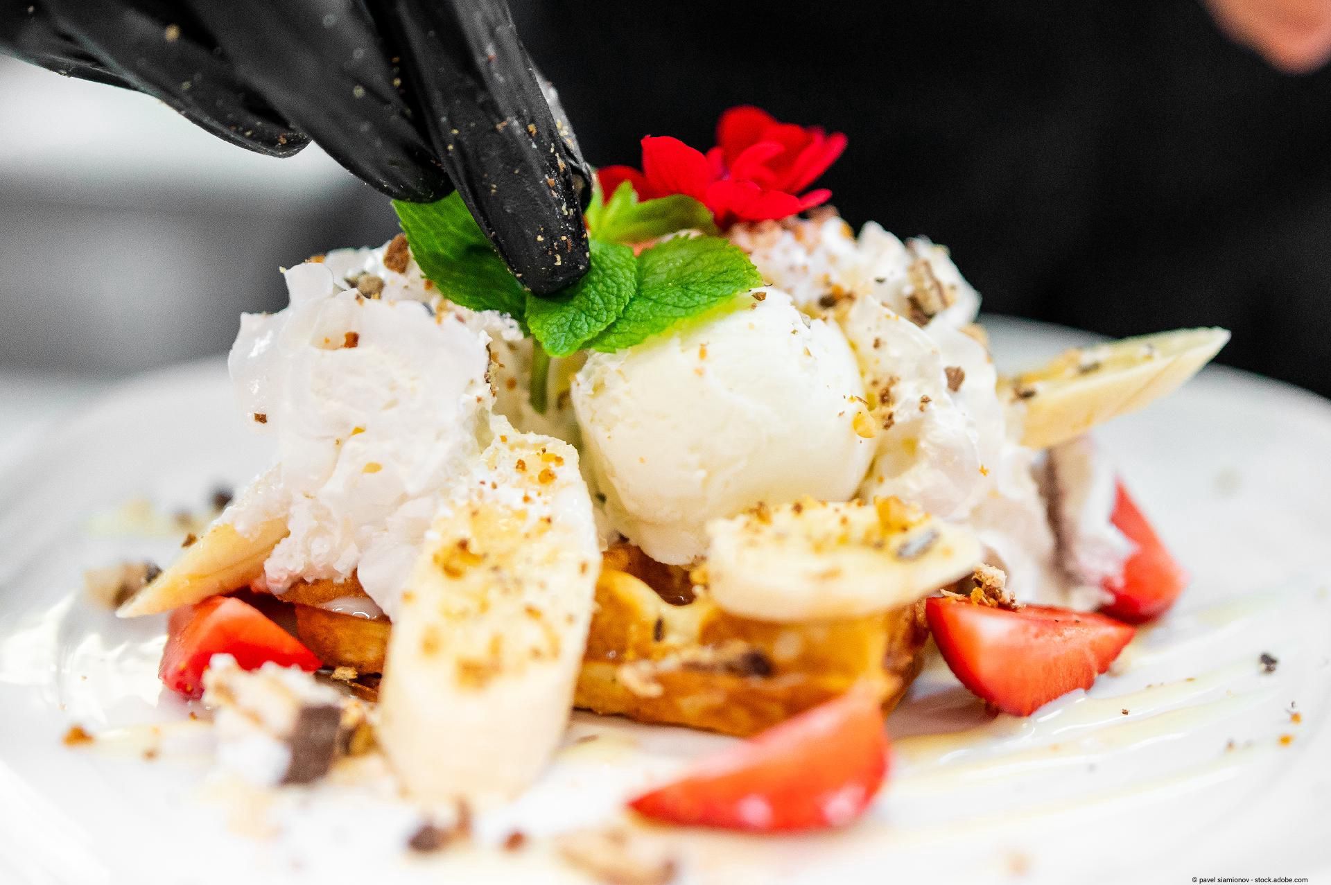 Ein Koch garniert ein aufwendiges Frühstücksgericht mit Minze, Ei und Erdbeeren